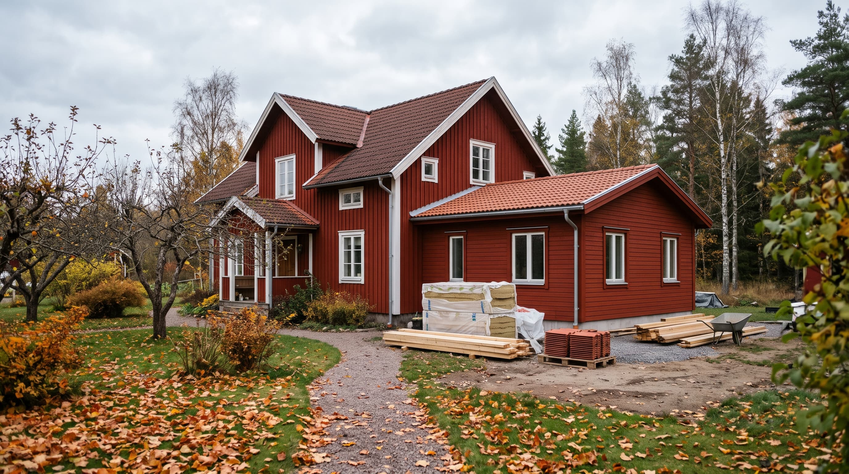 Rött trähus med vita knutar och nybyggd tillbyggnad, med isolering, virke och takpannor på gården en höstdag – tillbyggnader påverkar småhustaxeringen